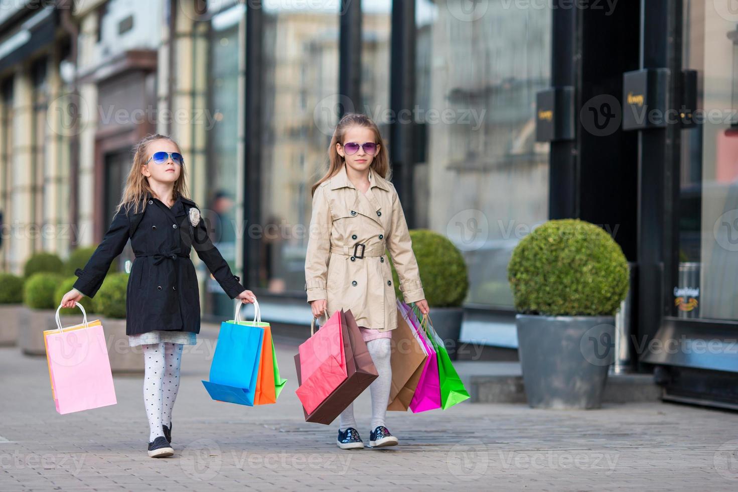 Adorable little girls with shopping bags walking in the city outdoors photo