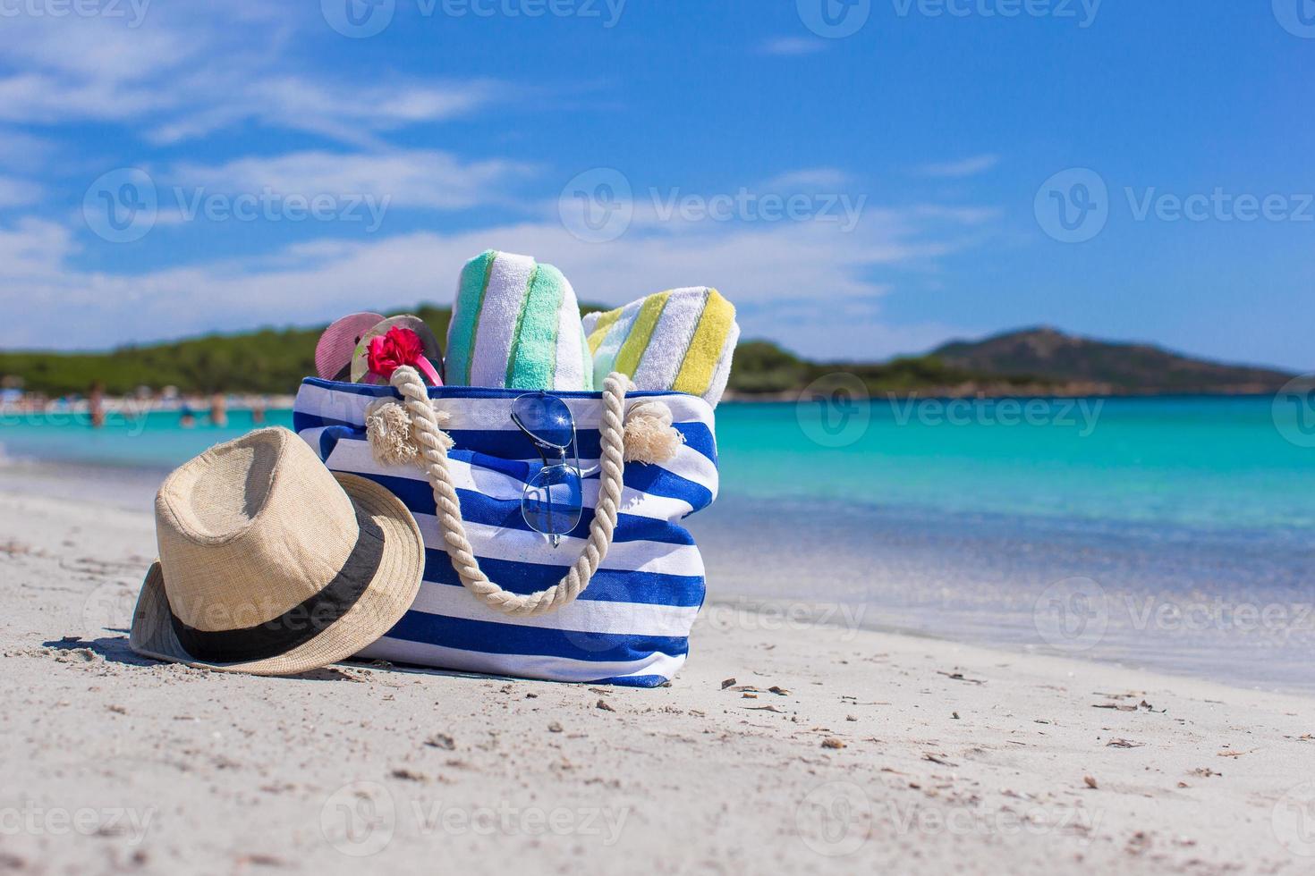 Blue bag, straw hat, flip flops and towel on white tropical beach photo