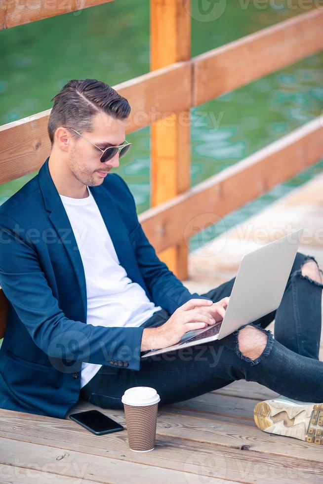 Closeup man hand working on wooden bridge with laptop, coffee and notebook photo