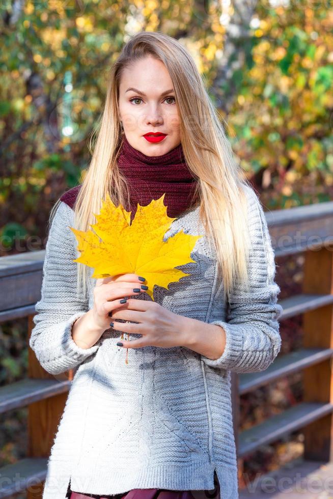 Fall concept - beautiful woman drinking coffee in autumn park under fall foliage photo