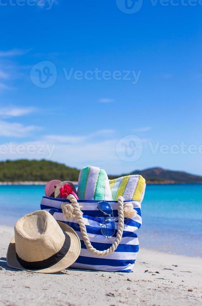 bolsa de rayas, sombrero de paja, bloqueador solar y frisbee en una playa tropical de arena blanca foto