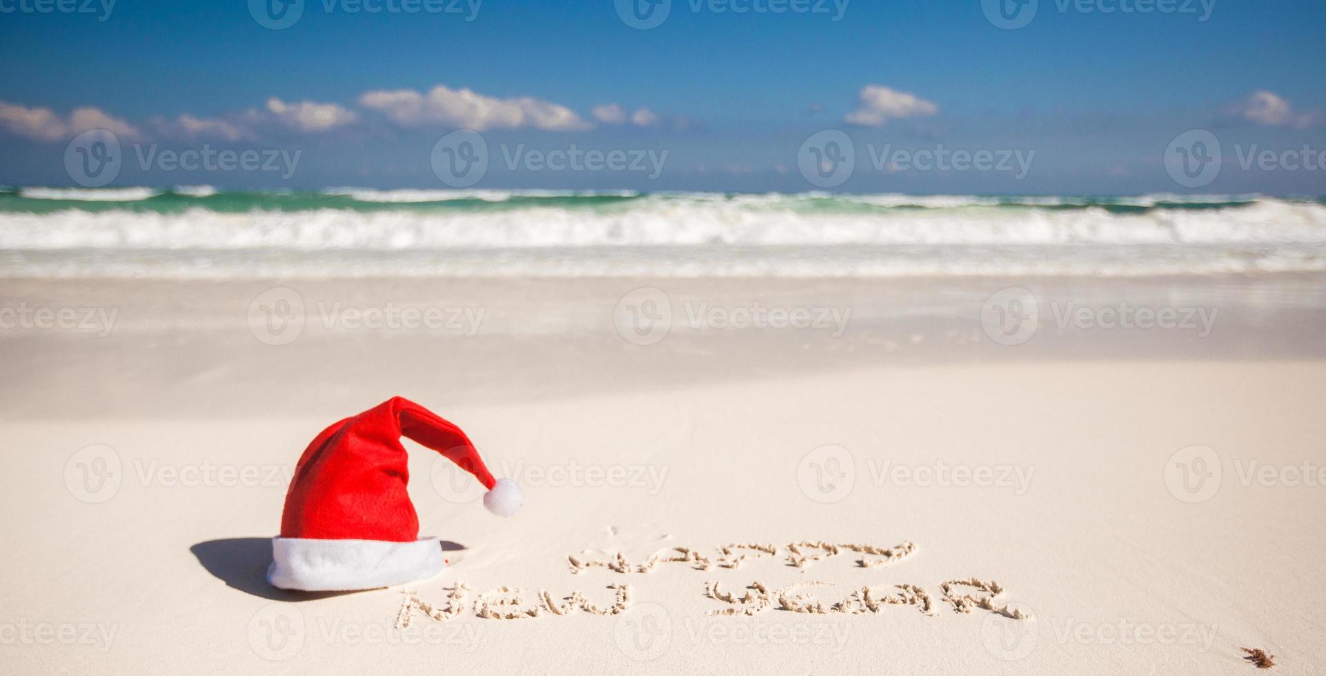 Happy New Year written in the sand and Santa Hat on white sandy beach photo