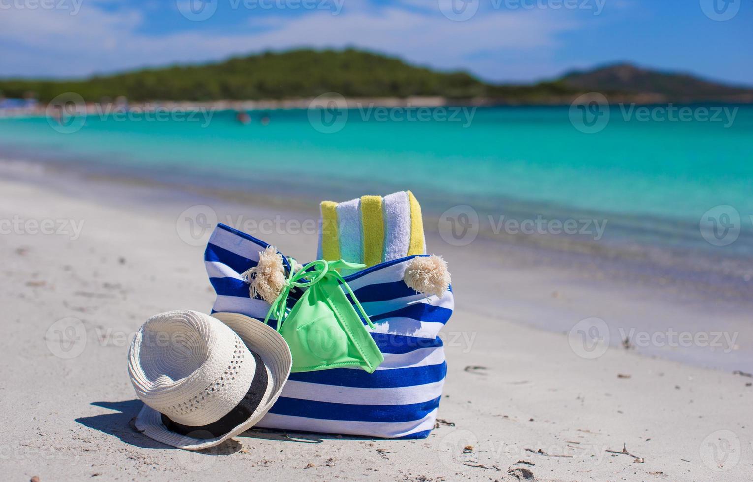bolsa de rayas, sombrero de paja, bloqueador solar y frisbee en una playa tropical de arena blanca foto