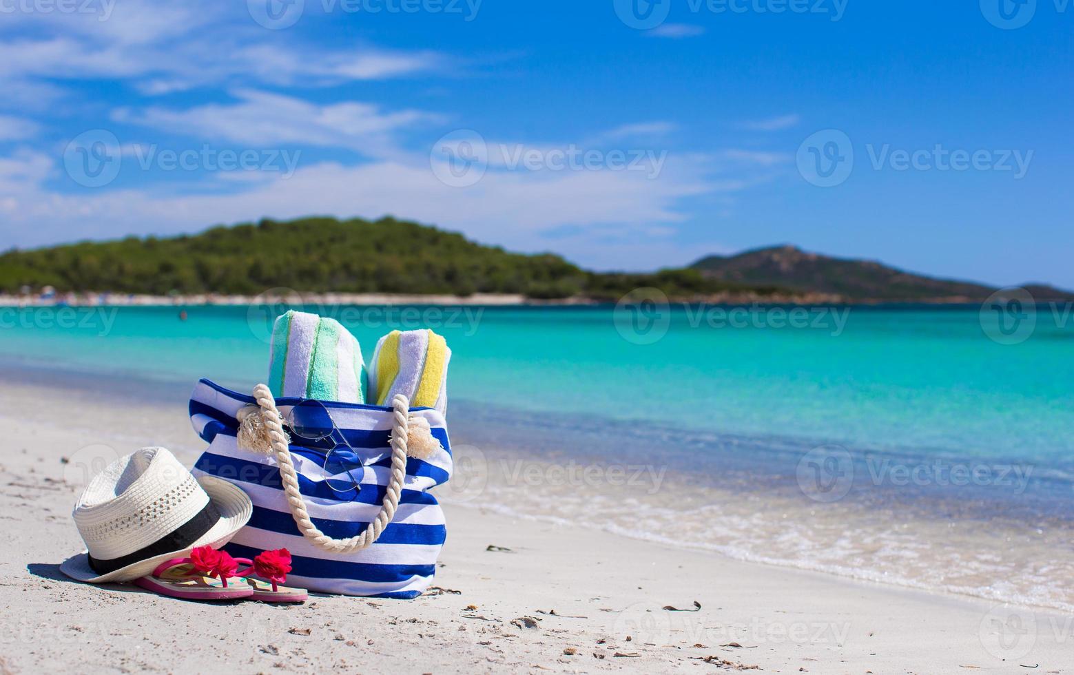 Stripe bag, straw hat, sunblock and frisbee on white sandy tropical beach photo