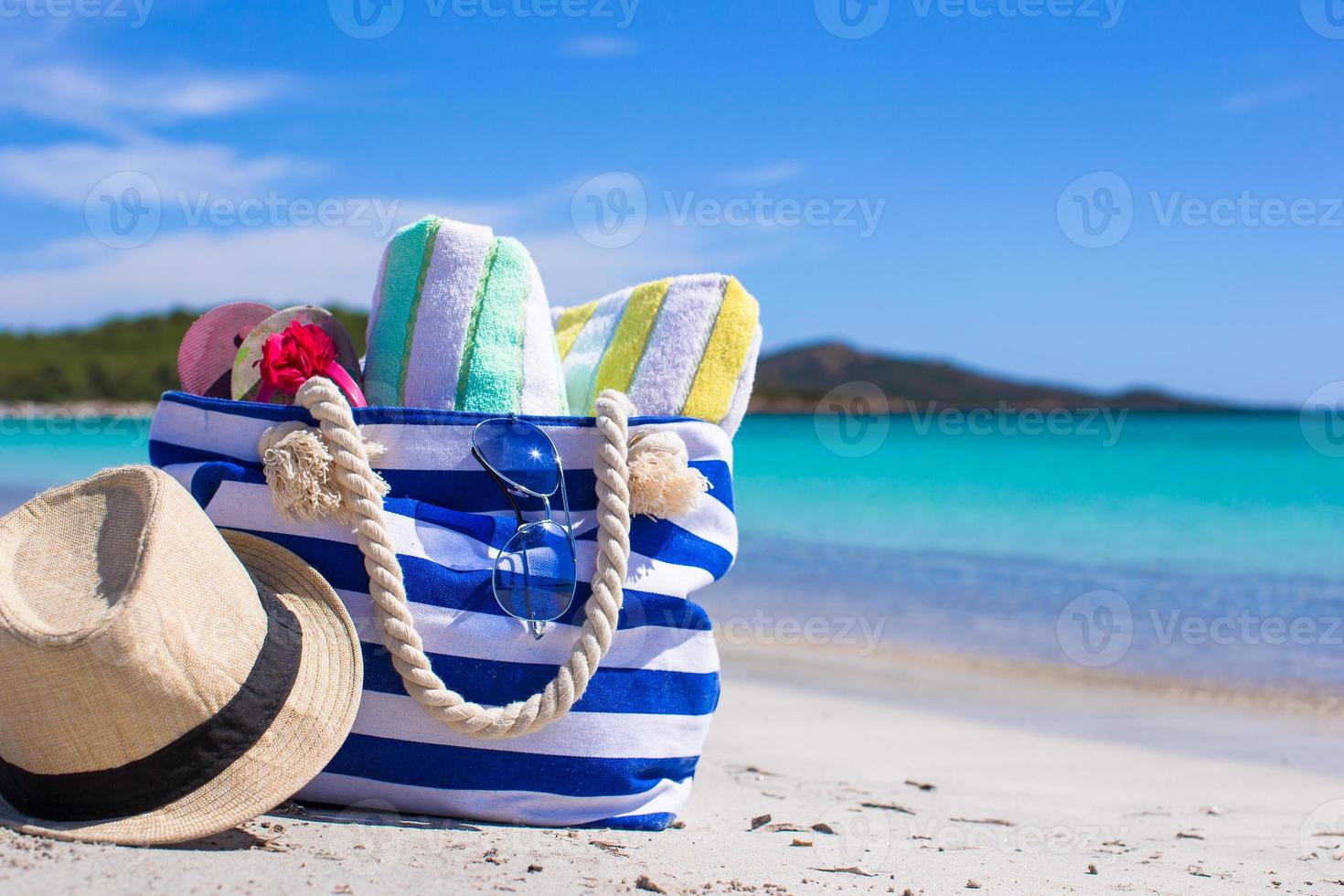 Stripe bag, straw hat, sunblock and frisbee on white sandy tropical beach photo