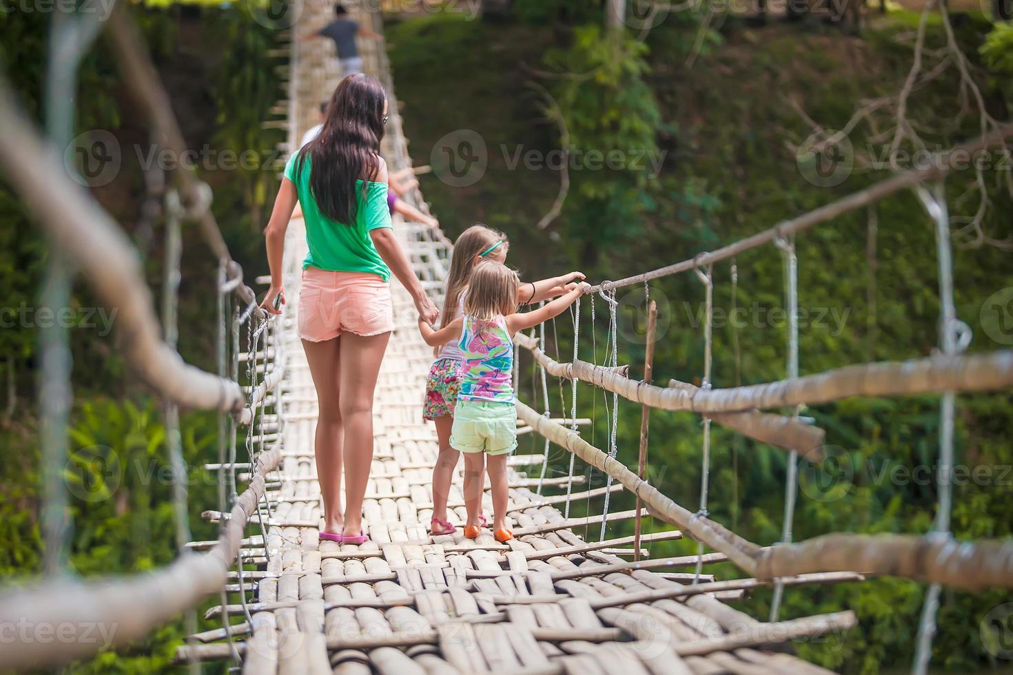 Back view of little girls and young woman walking on suspension bridge over the River Loboc, Philippines photo