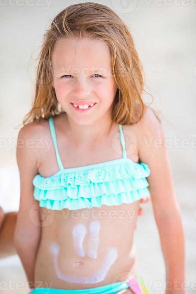 Little girl having fun at tropical beach on lounger with smile painting by suncream photo