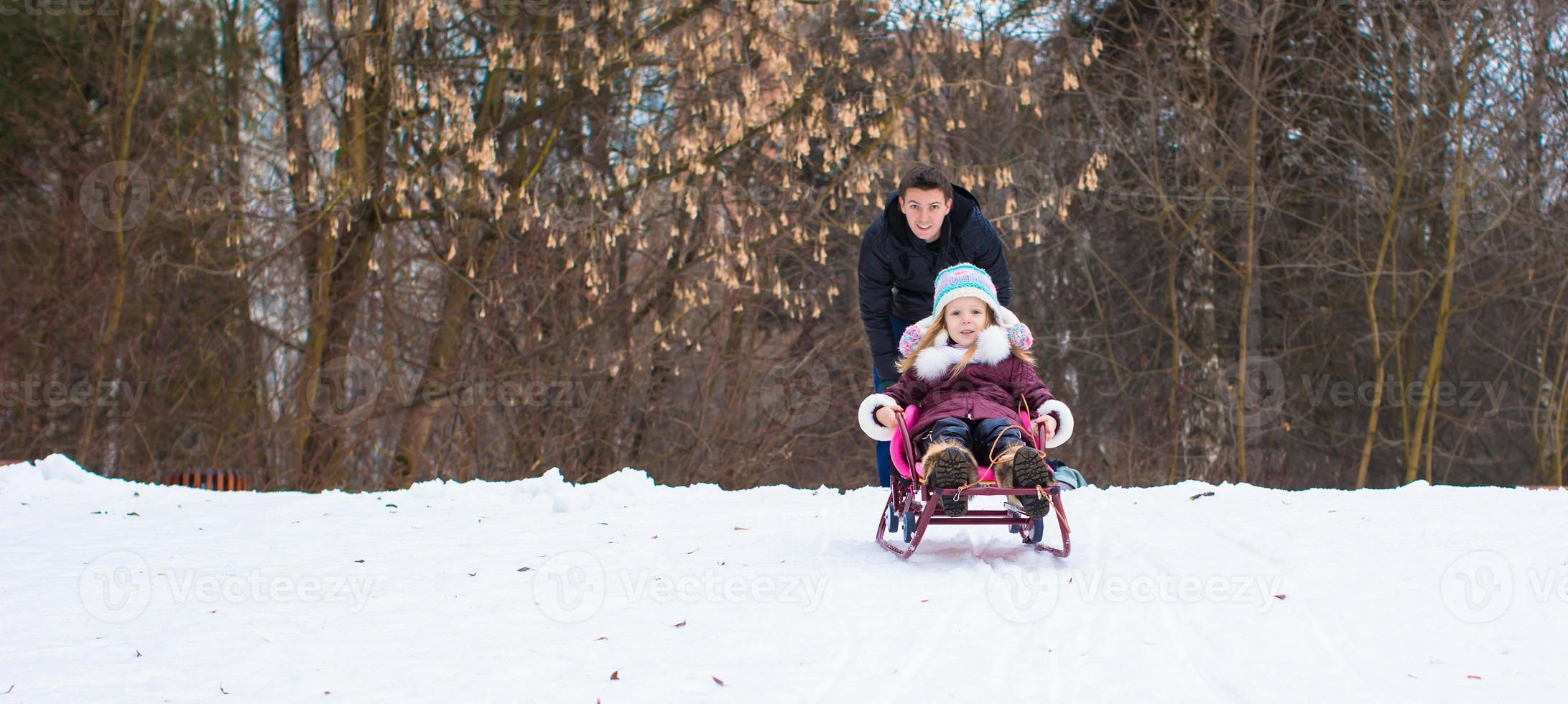 niña y padre feliz paseando en trineo en un día nevado de invierno foto