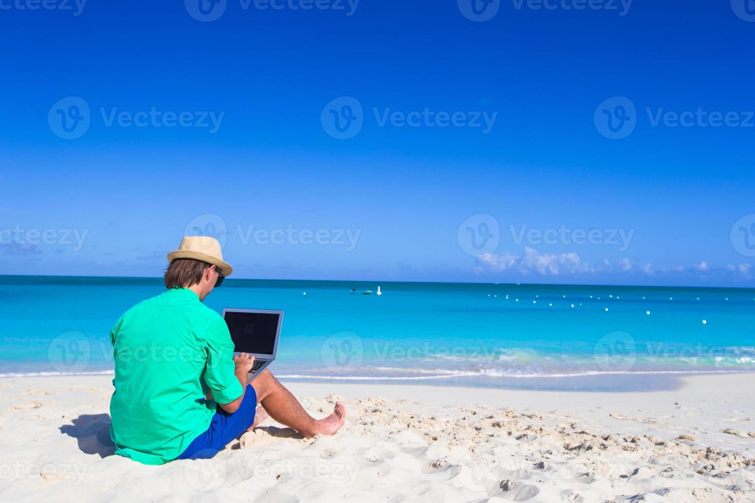 Young man working on laptop at tropical beach photo