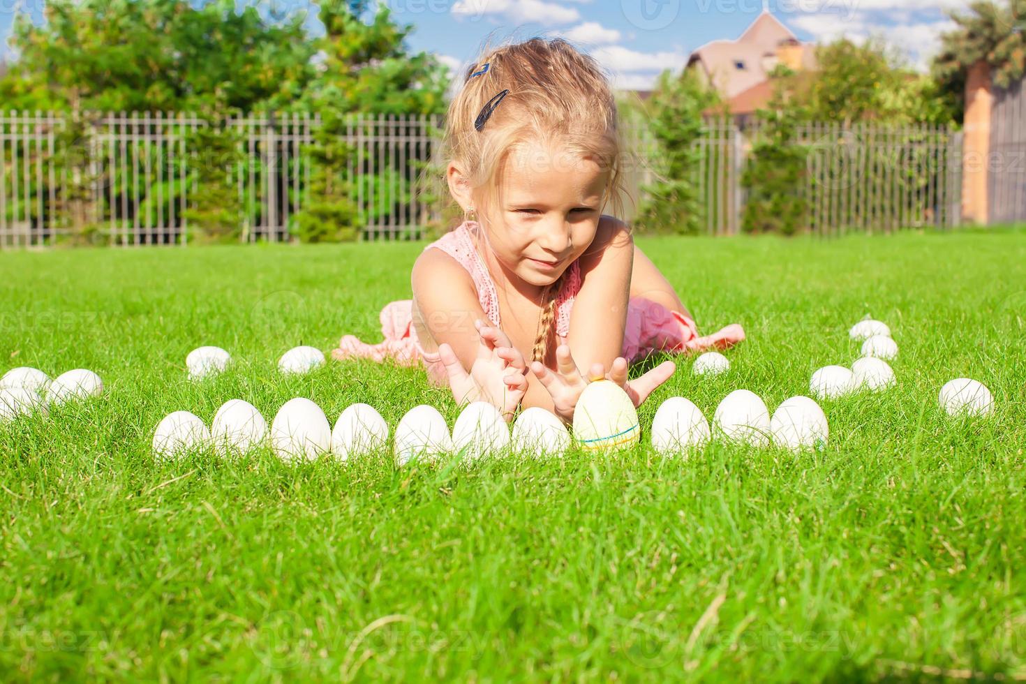 Portrait of little adorable girl playing with white Easter eggs in the yard photo