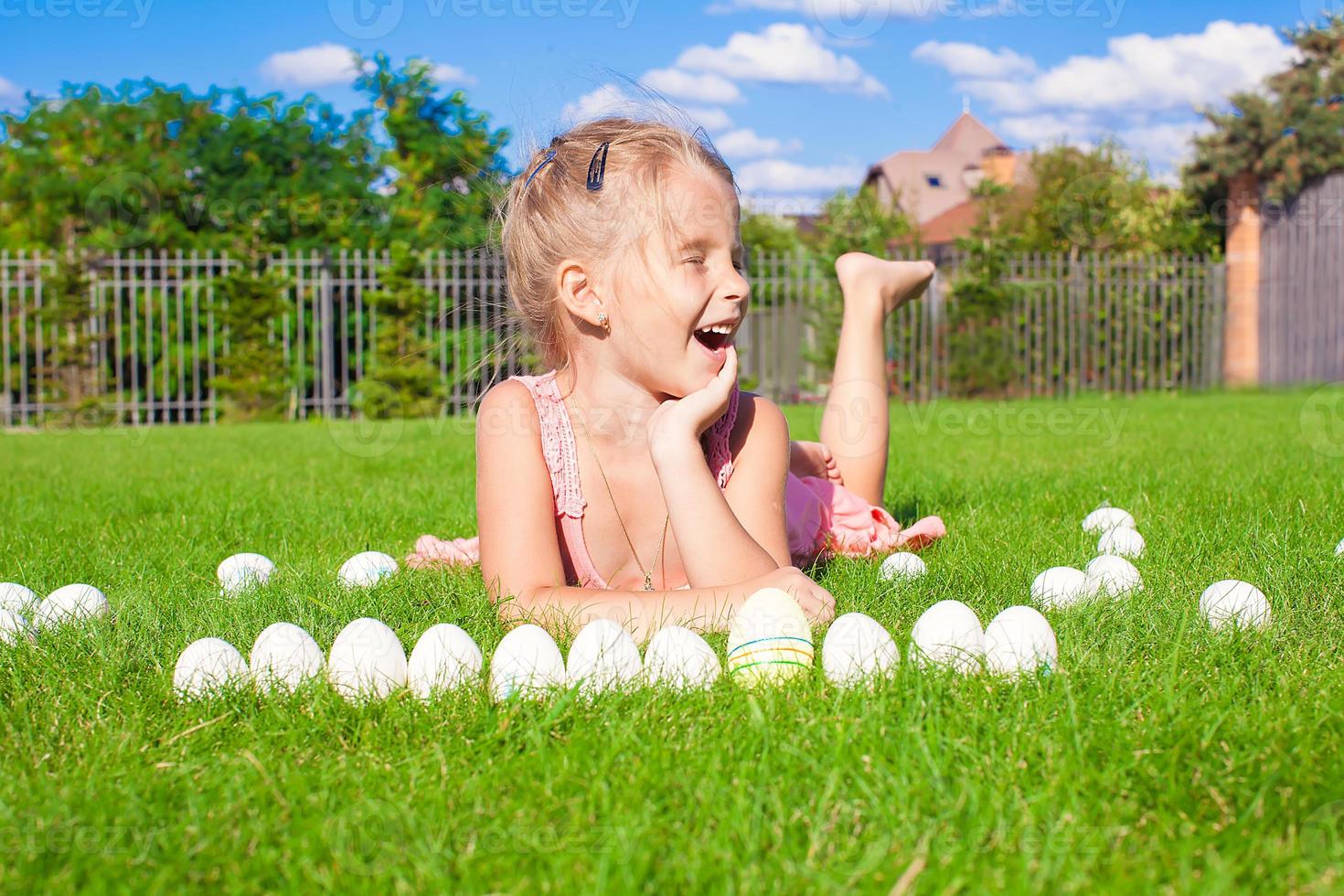 Little happy girl playing with white Easter eggs on green grass photo