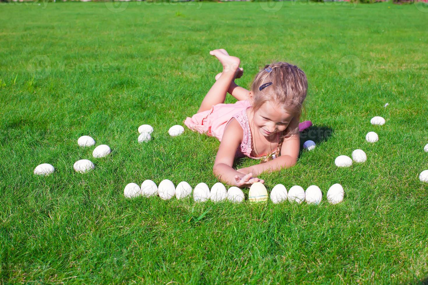 niña feliz jugando con huevos de pascua blancos sobre hierba verde foto