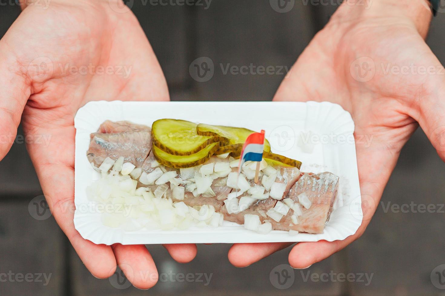 Tasty fresh herring with onion and netherland flag on the water channel background in Amsterdam. Traditional dutch food photo