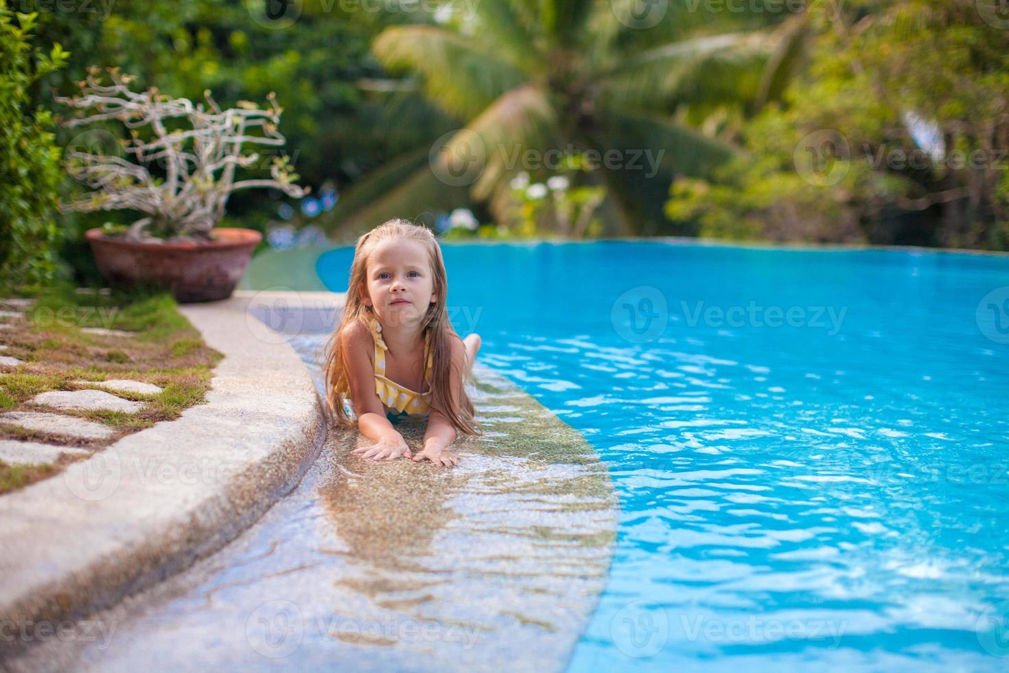 Little adorable girl in the swimming pool looks at camera photo