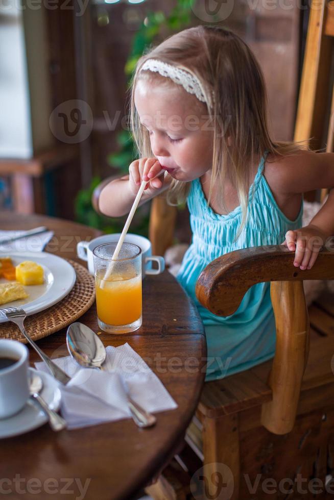 Adorable little girl having breakfast and drinking fruit cocktail photo