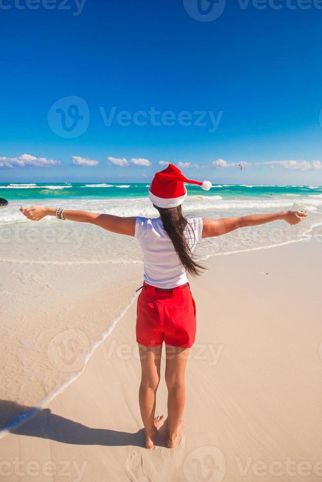 Young woman in Santa Hat walking spread her hands on white sandy beach photo