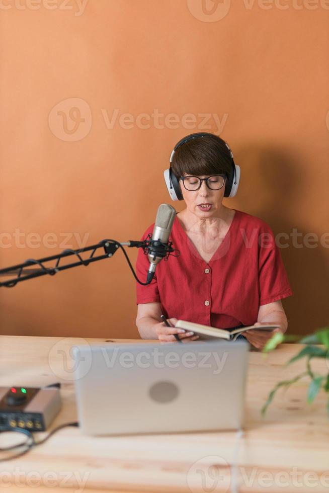 Portrait of mature woman wearing headphones and talking at online radio station - podcast and broadcast concept photo