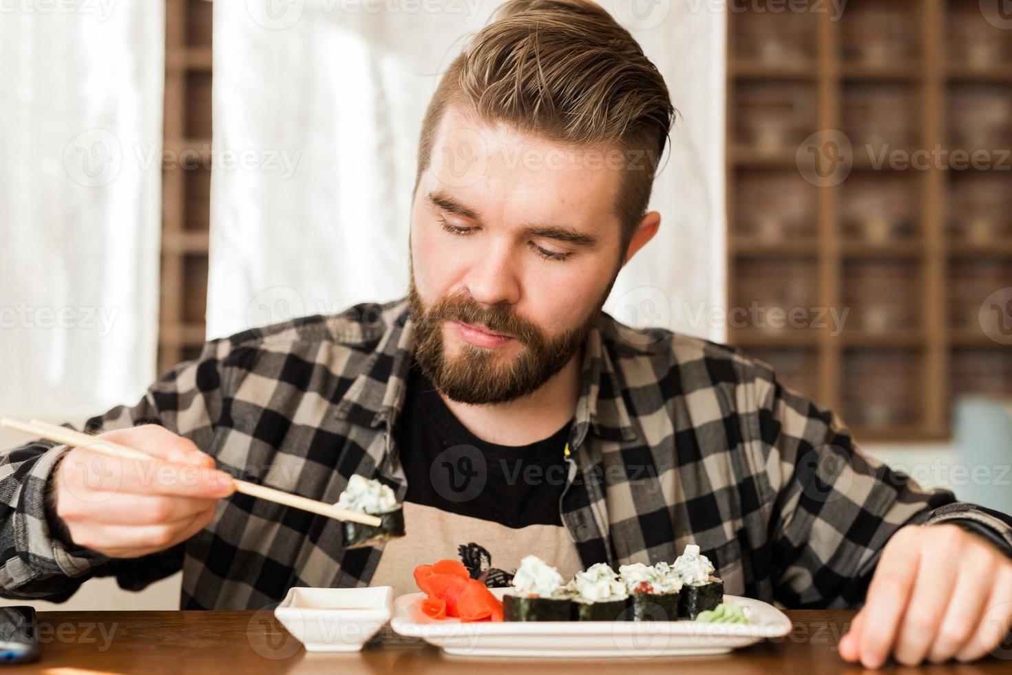 Man eating sushi rolls using bamboo sticks in a restaurant. Japanese cuisine photo