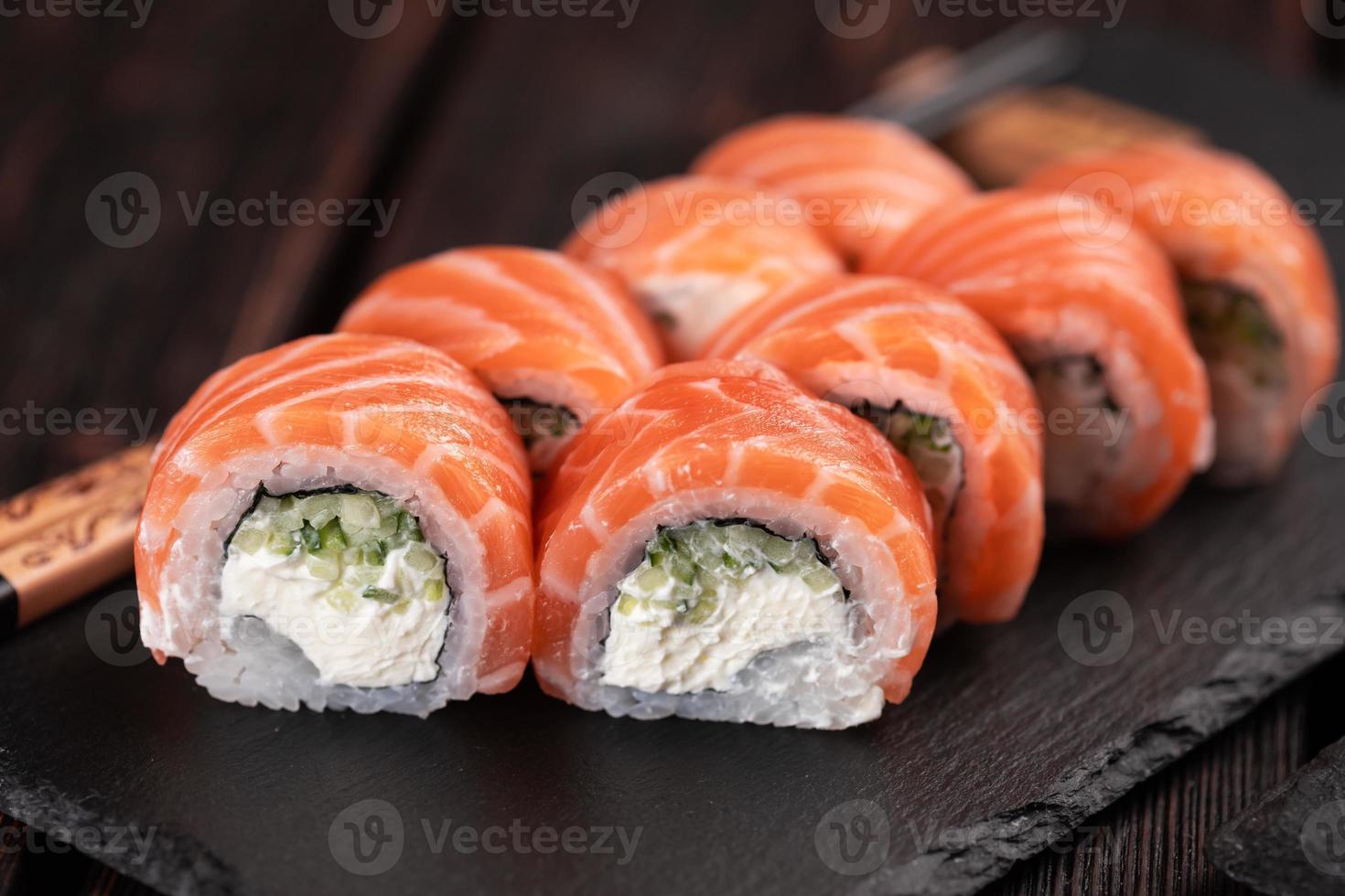 sushi roll philadelphia con salmón y pepino y queso crema en primer plano de fondo negro. menú de sushi concepto de comida japonesa foto