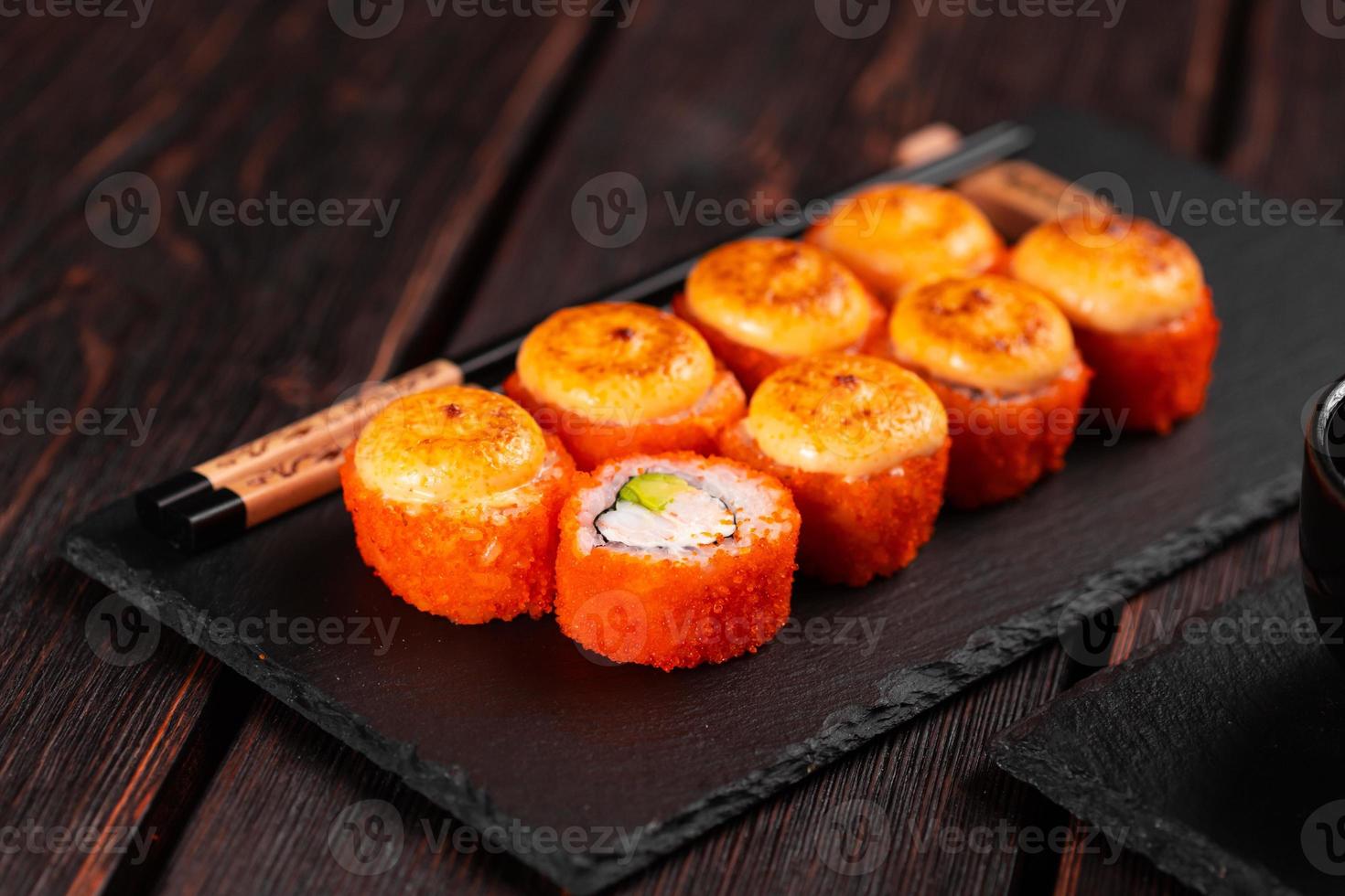 Sushi roll with crab, avocado and tobiko caviar served on black board close-up - Japanese asian food photo