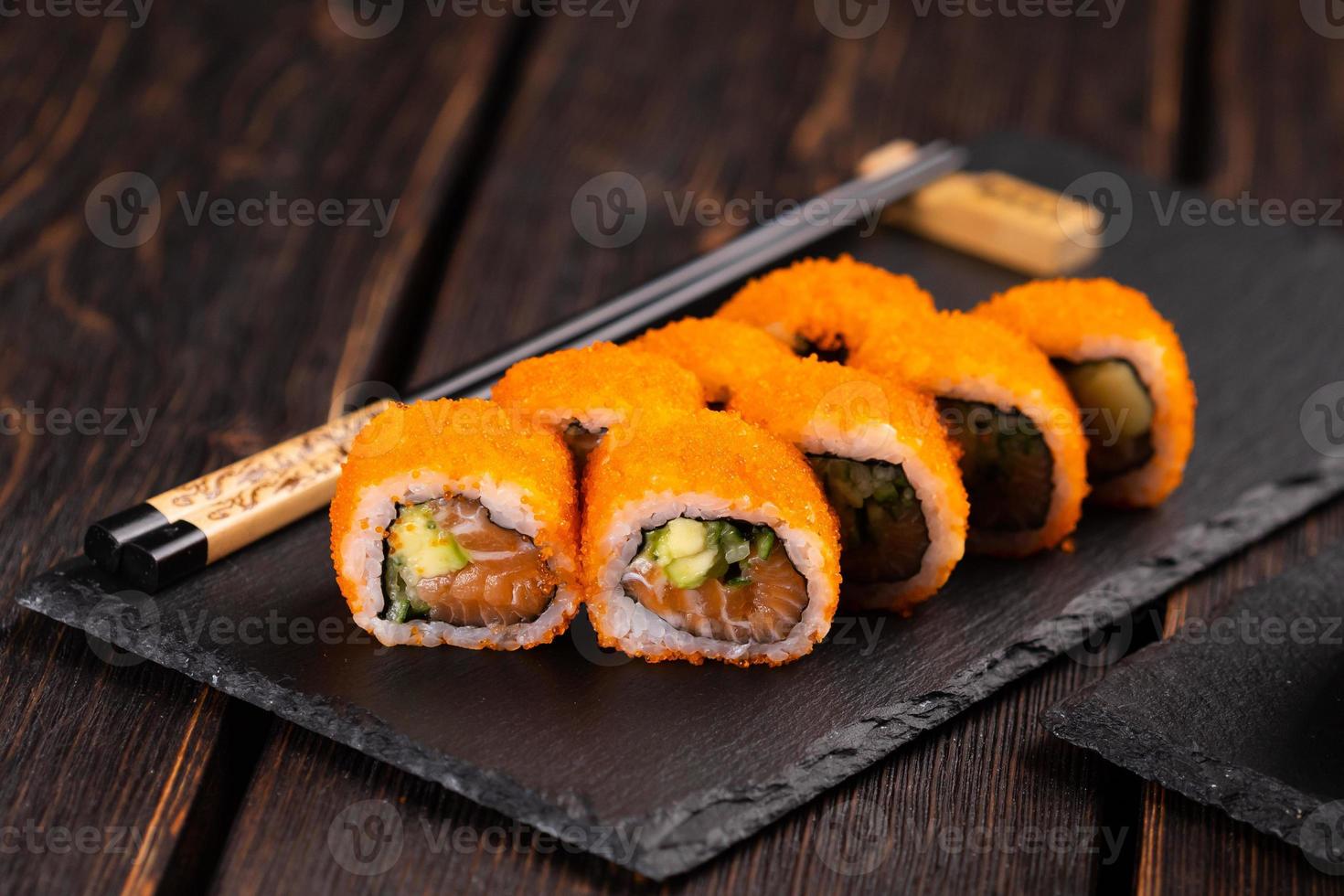 rollo de sushi de california con salmón, aguacate, pepino y caviar tobiko servido en el primer plano de la pizarra negra - comida japonesa foto