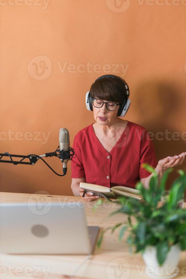 Mature woman making podcast recording for her online show. Attractive business woman using headphones front of microphone for a radio broadcast photo