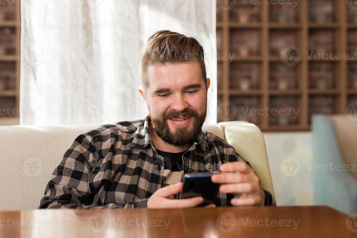 Man holding modern digital smartphone device and chatting in social networks. Guy sending message on cellular while sitting at table in cafe photo