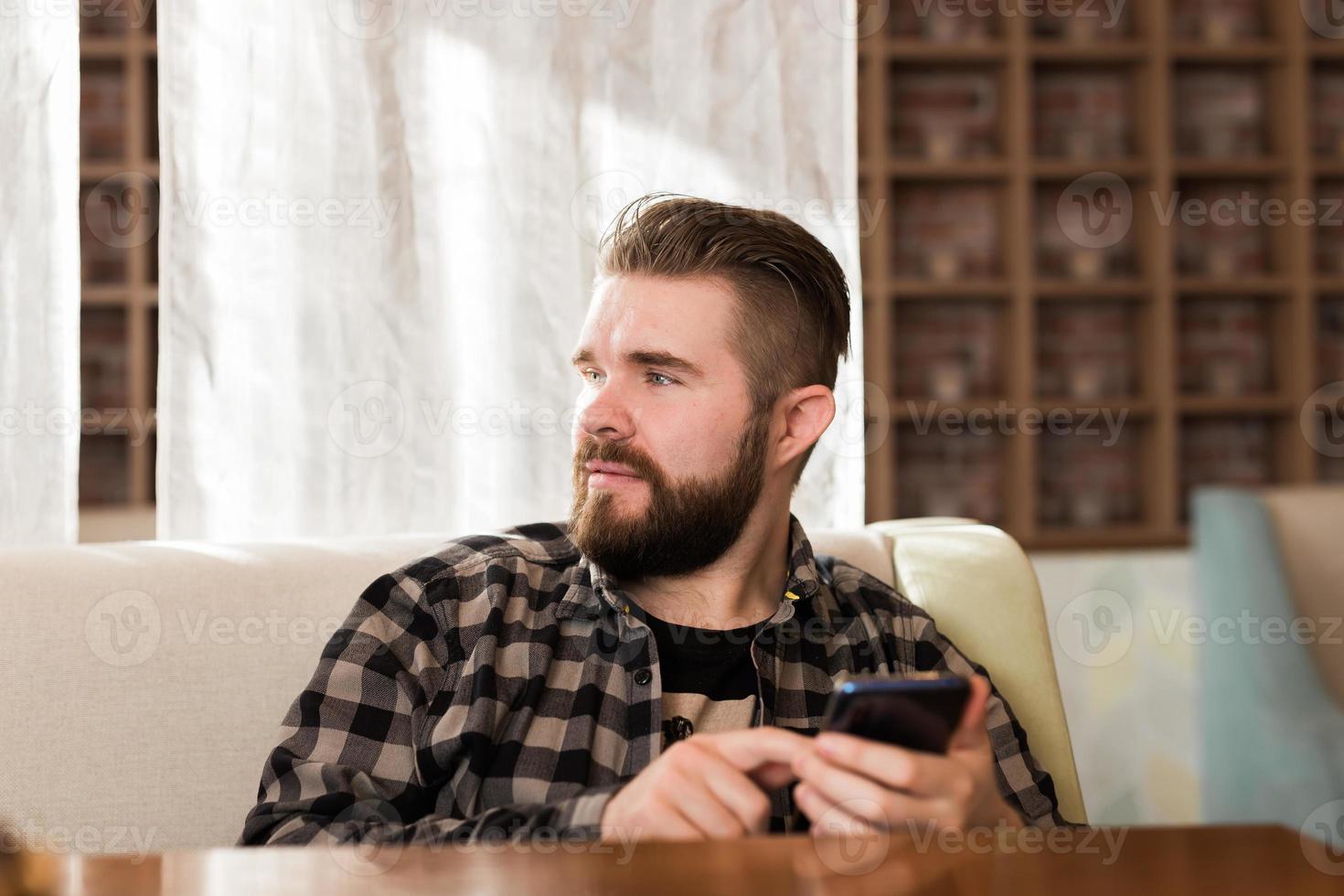 Man holding modern digital smartphone device and chatting in social networks. Guy sending message on cellular while sitting at table in cafe photo