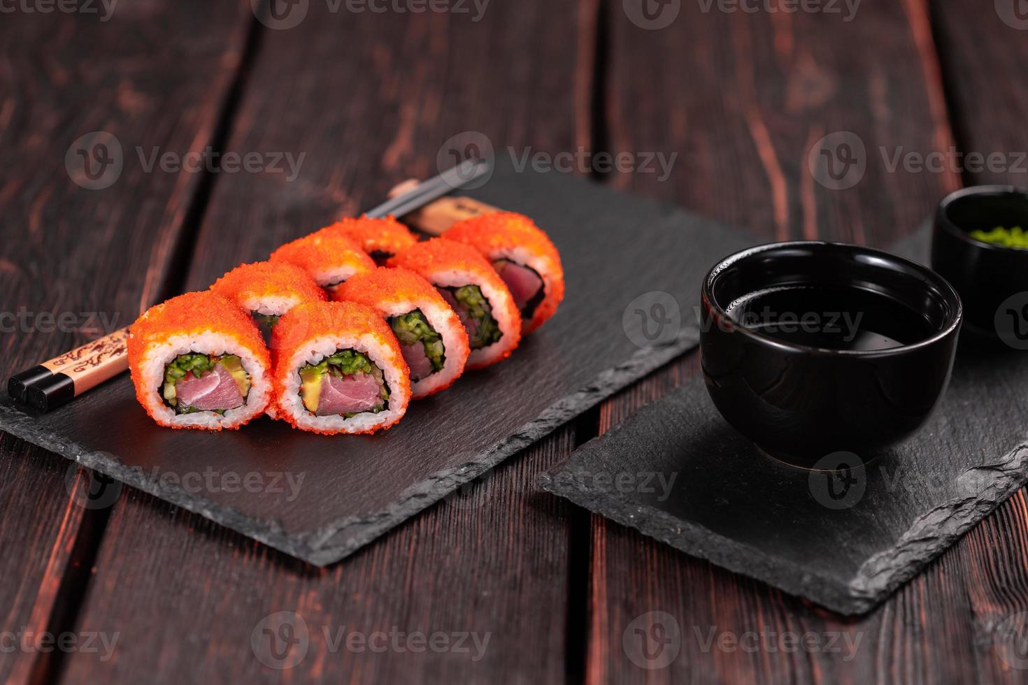 rollo de sushi de california con atún, pepino de aguacate y caviar de tobiko servido en el primer plano de la pizarra negra - comida japonesa foto