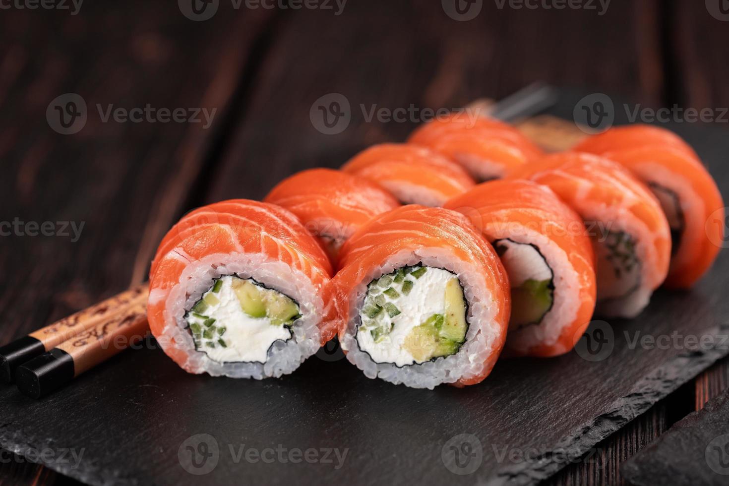 Sushi roll philadelphia with salmon and cucumber with avocado and cream cheese on black background. Sushi menu. Japanese food concept photo