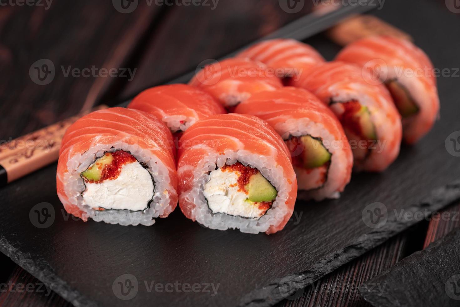 rollo de sushi maguro con salmón, aguacate y tobiko, queso filadelfia en primer plano de pizarra negra. menú de sushi comida japonesa. foto