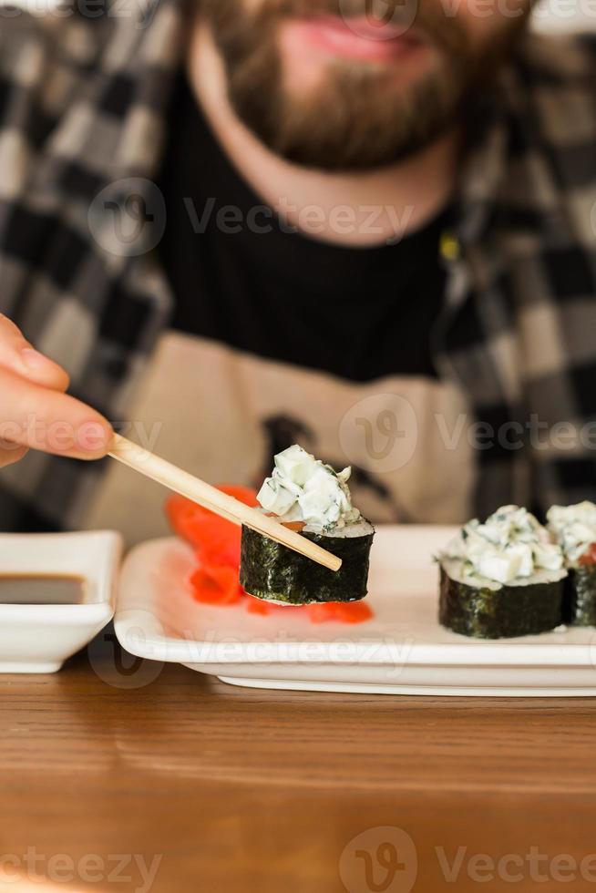 Close up of sushi rolls on a table in a restaurant. Man eating sushi rolls using bamboo sticks. Japanese cuisine photo