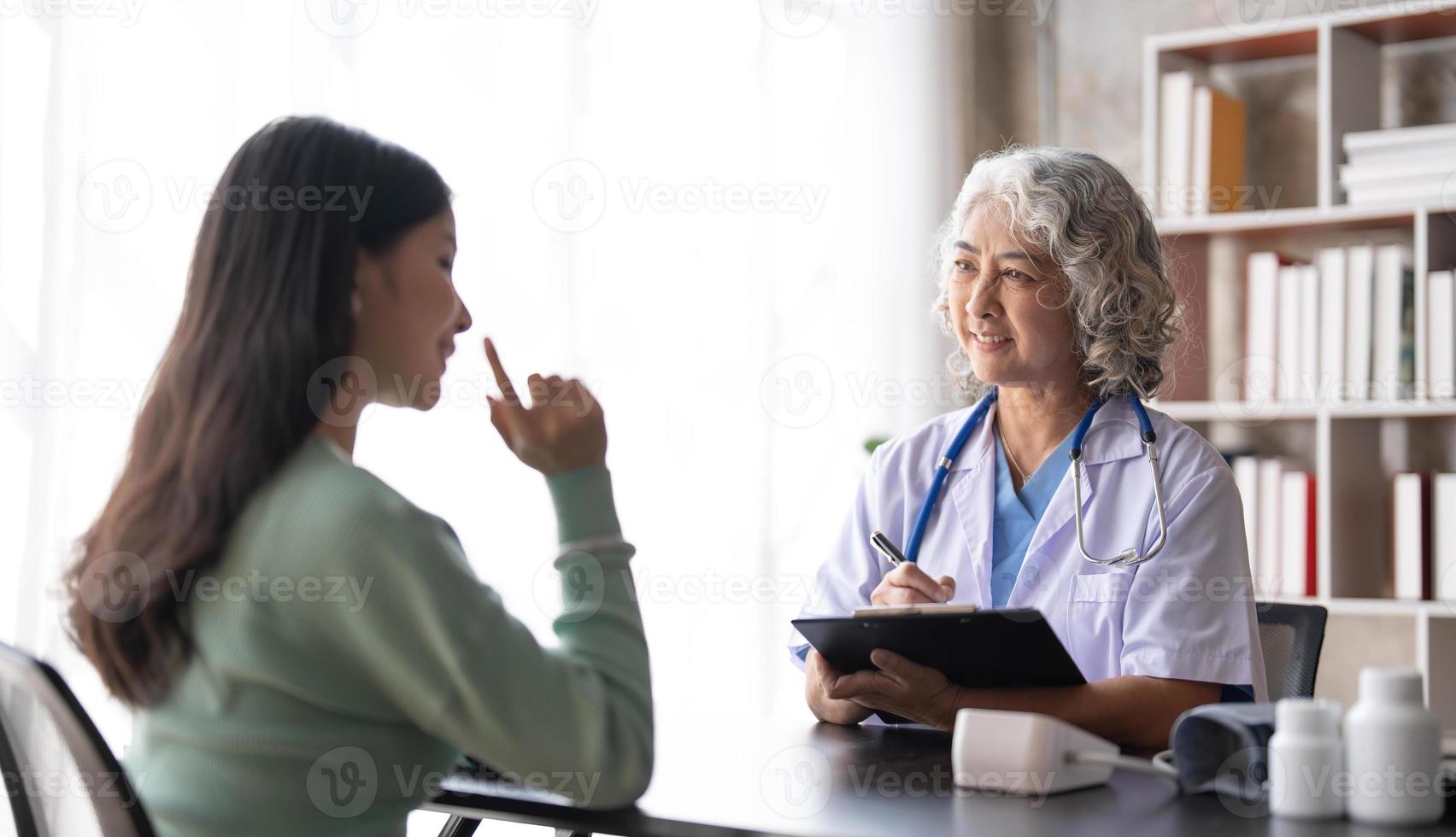 una doctora principal está leyendo el historial médico de una paciente y hablando con ella durante la consulta en una clínica de salud. médico en bata de laboratorio sentado detrás de una computadora portátil en la oficina del hospital. foto