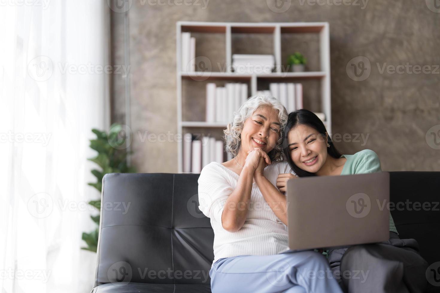 Mature mother grown up daughter sit on couch in living room hold on lap pc looking at screen watching movie film, using device make video call, shopping via e-commerce website, girl teach mom concept photo