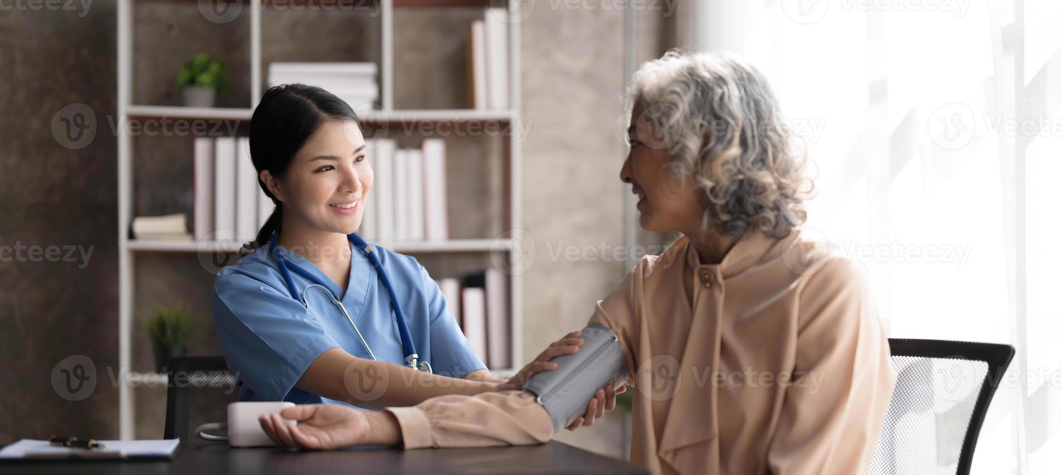 Female nurse doing blood pressure measurement of a senior woman patient. Doctor checking blood pressure of an elderly woman at old age home. Female caregiver and senior woman together at home photo