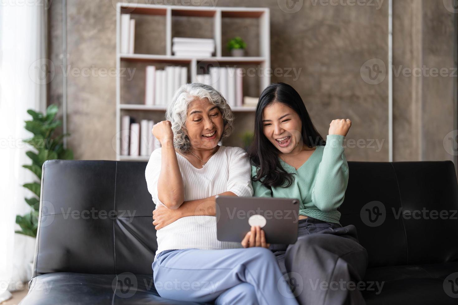 Mature mother grown up daughter sit on couch in living room hold on lap pc looking at screen watching movie film, using device make video call, shopping via e-commerce website, girl teach mom concept photo