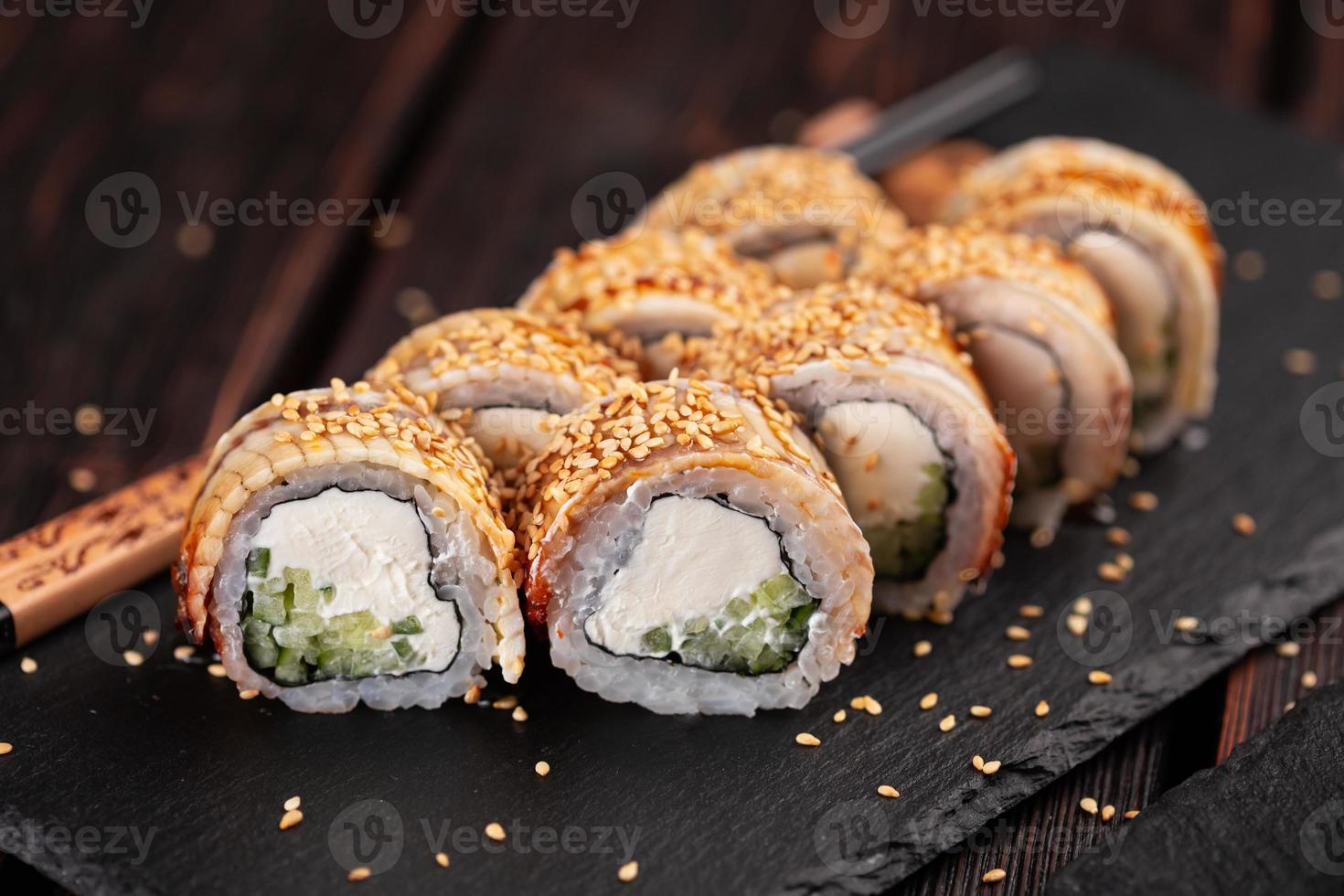 Japanese cuisine - sushi roll with cucumber and cream cheese topped with eel close-up on black board photo