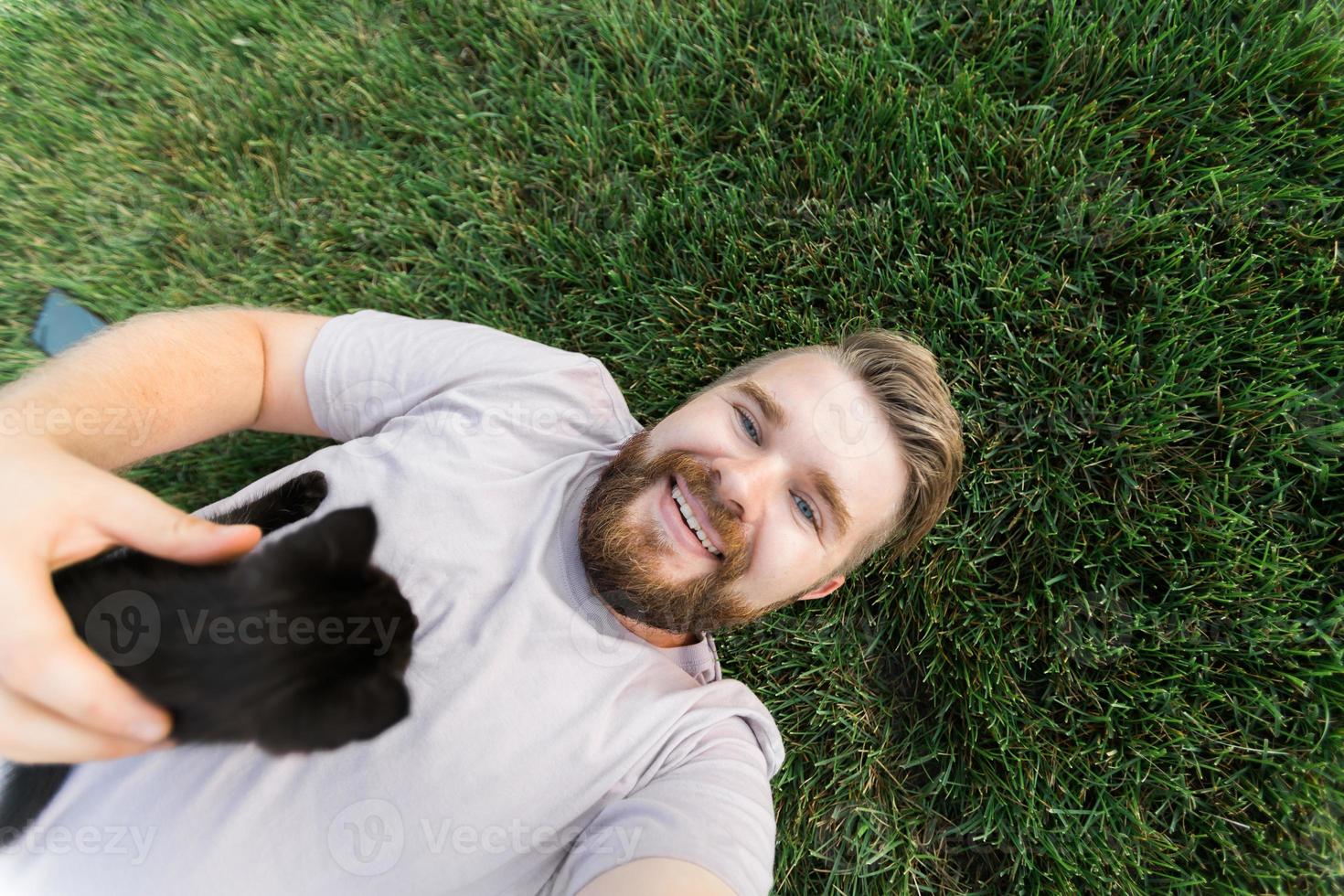 Man with little kitten lying and playing on grass - friendship love animals and pet owner concept photo