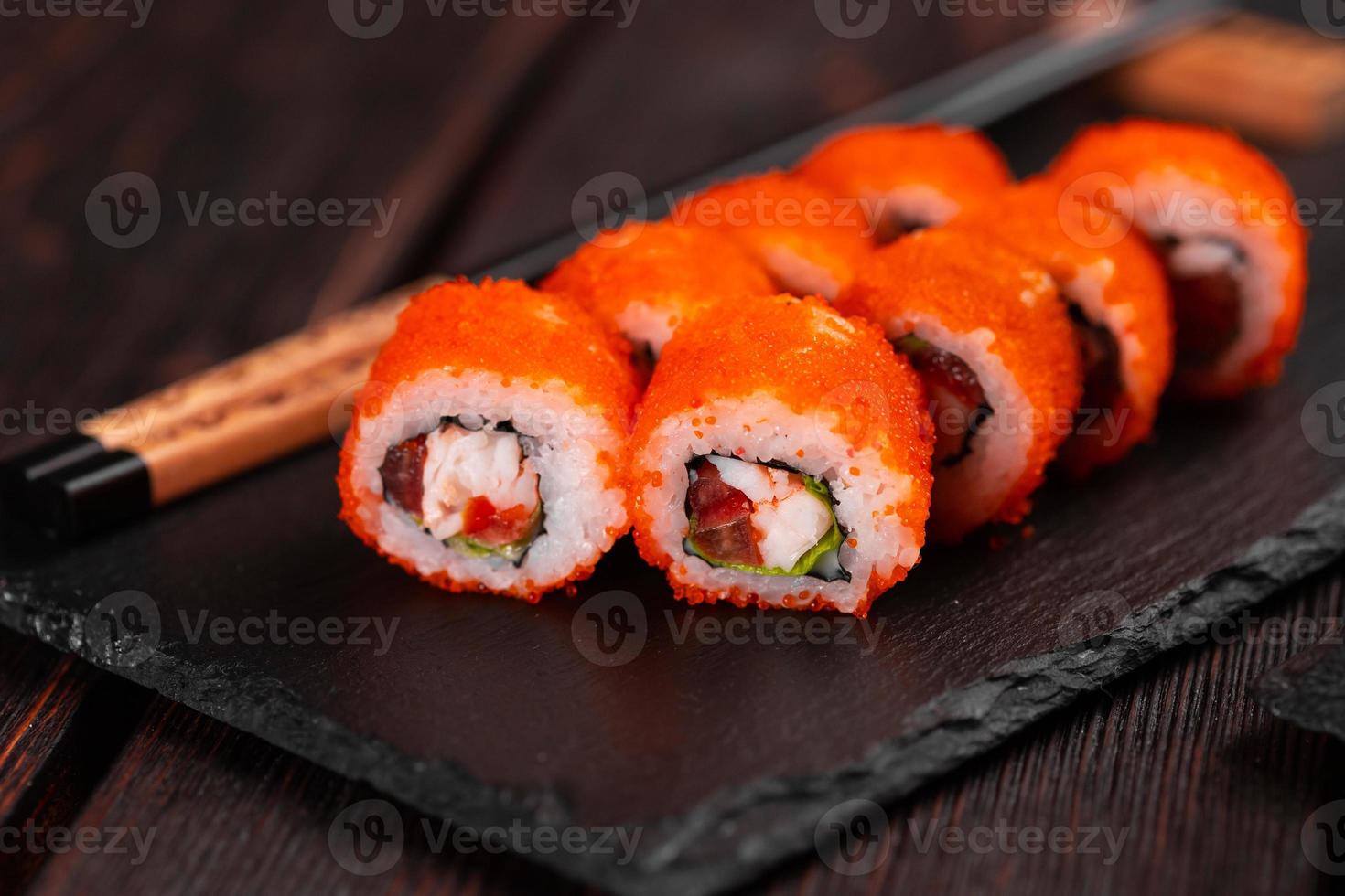 rollo de sushi con camarones y pimiento rojo y caviar tobiko con ensalada servida en el primer plano de la pizarra negra - comida japonesa foto