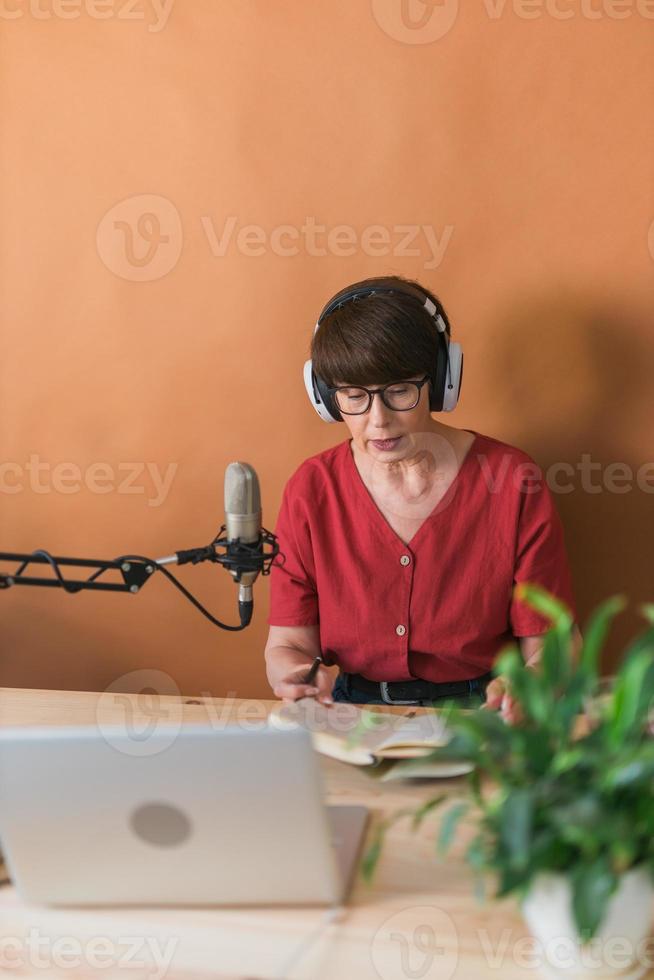 presentadora de radio de mediana edad hablando en el micrófono y leyendo noticias - concepto de transmisión de radio en línea foto