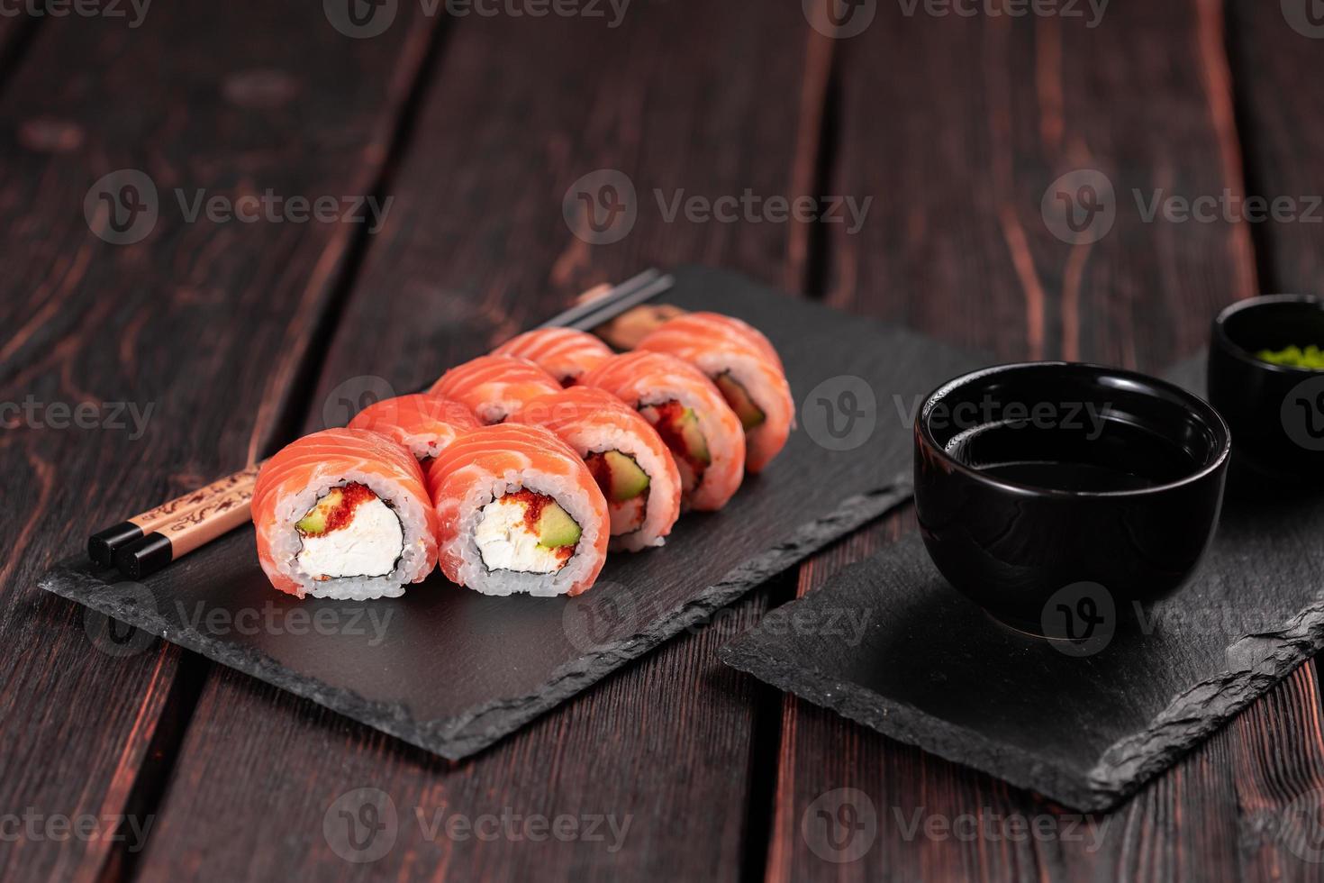 rollo de sushi maguro con salmón, aguacate y tobiko, queso filadelfia en primer plano de pizarra negra. menú de sushi comida japonesa. foto