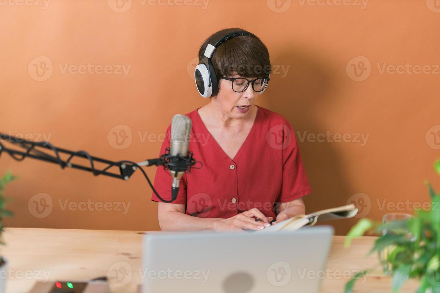 Middle-aged female radio presenter talking into the microphone and reading news - radio broadcast online concept photo