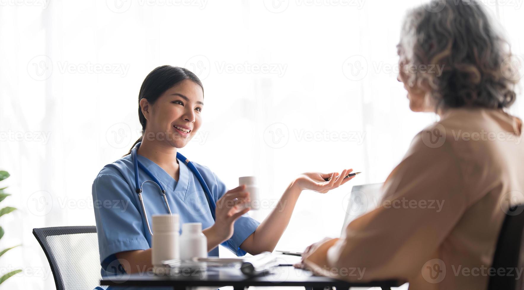 Asian Senior elderly female patient consult with physician nurse at nursing home care. Caregiver therapist pharmacist girl hold medicine pills bottle, explain prescription to older disabled guy photo