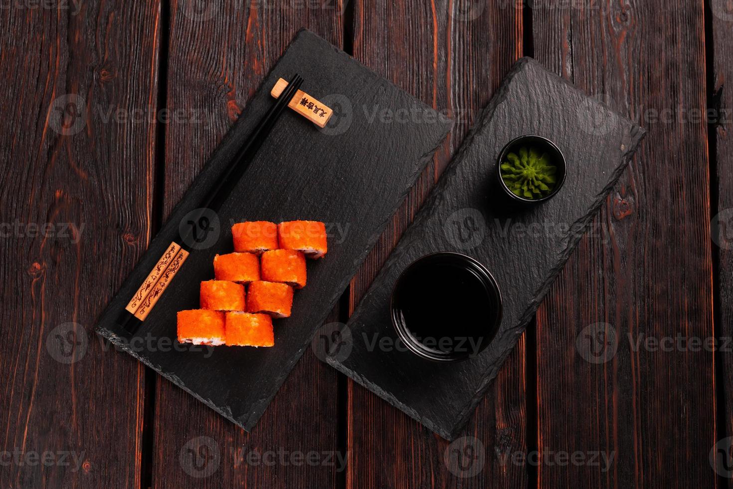 Sushi roll with shrimp and red pepper and tobiko caviar with salad served on black board top view - Japanese food photo