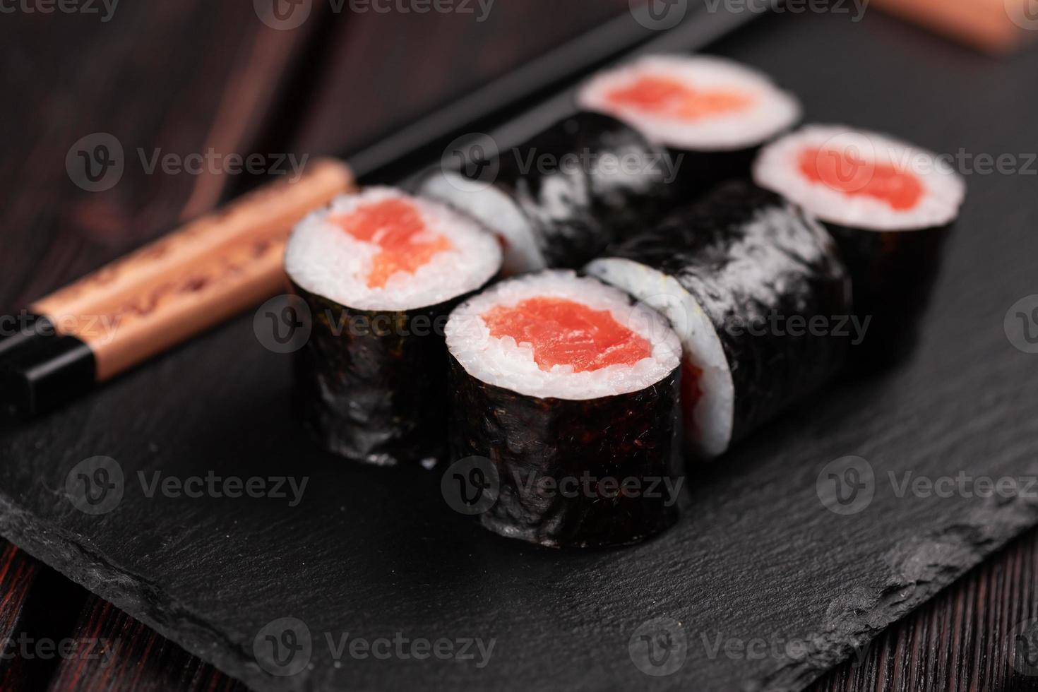 Maki sushi roll with salmon avocado and tobiko caviar served on black board close-up - Japanese food photo