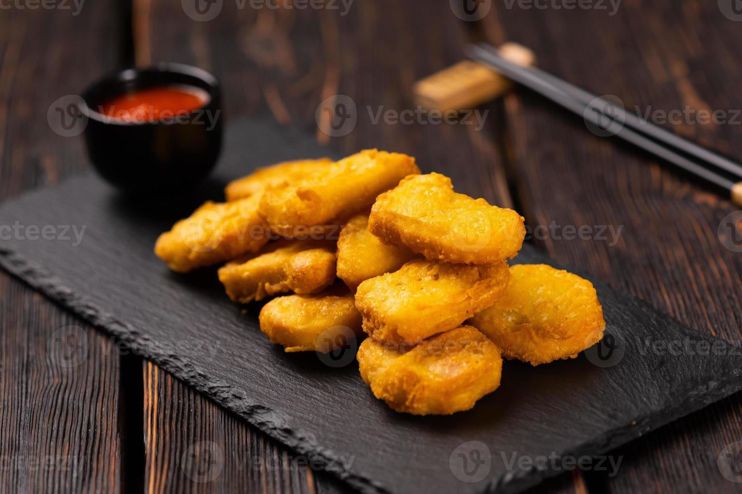 Fried chicken pieces on stone board with chopsticks - asian food close-up photo