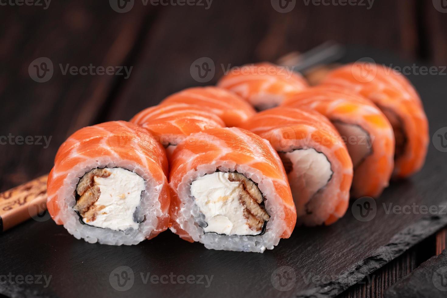 sushi roll philadelphia con salmón y anguila y queso crema en primer plano de fondo negro. menú de sushi concepto de comida japonesa foto