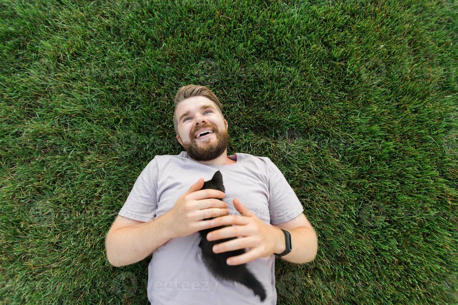 Man with little kitten lying and playing on grass - friendship love animals and pet owner concept photo