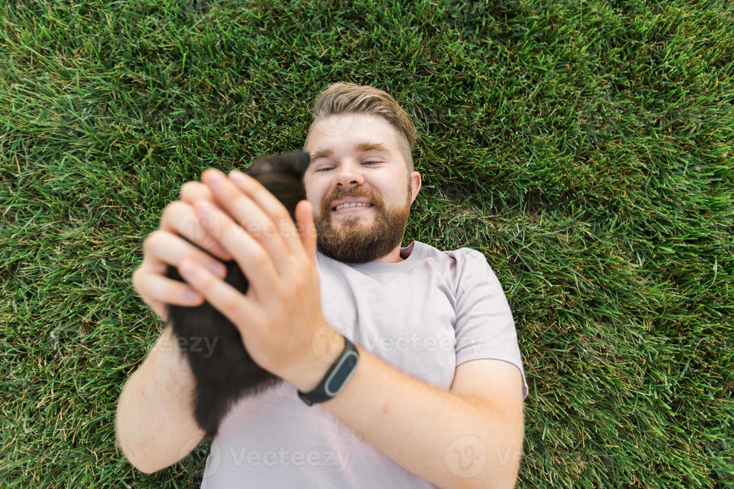 Man with little kitten lying and playing on grass - friendship love animals and pet owner concept photo