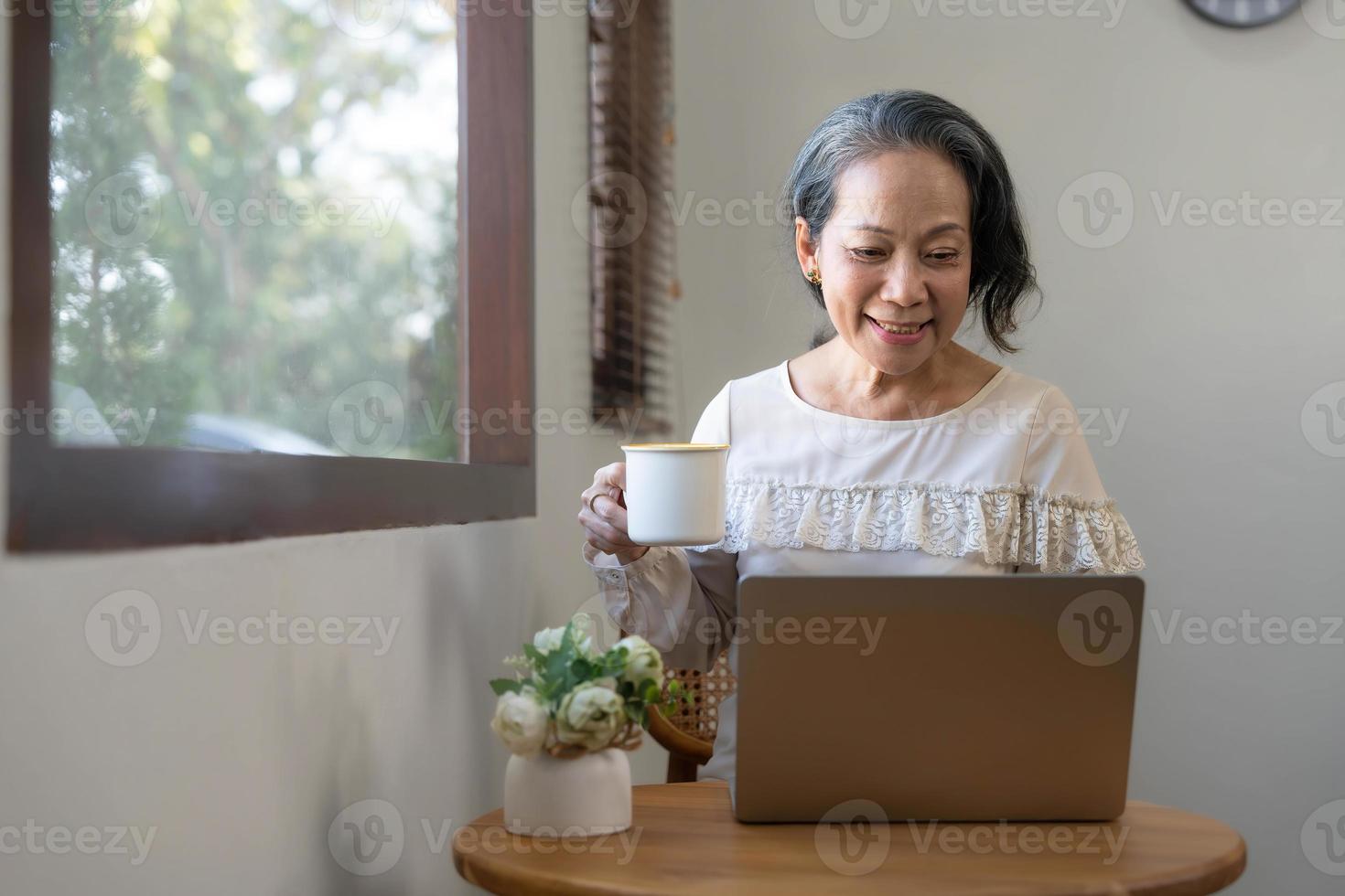 Portrait, Professional and successful aged Asian businesswoman working from home, sipping morning coffee while using laptop computer. photo